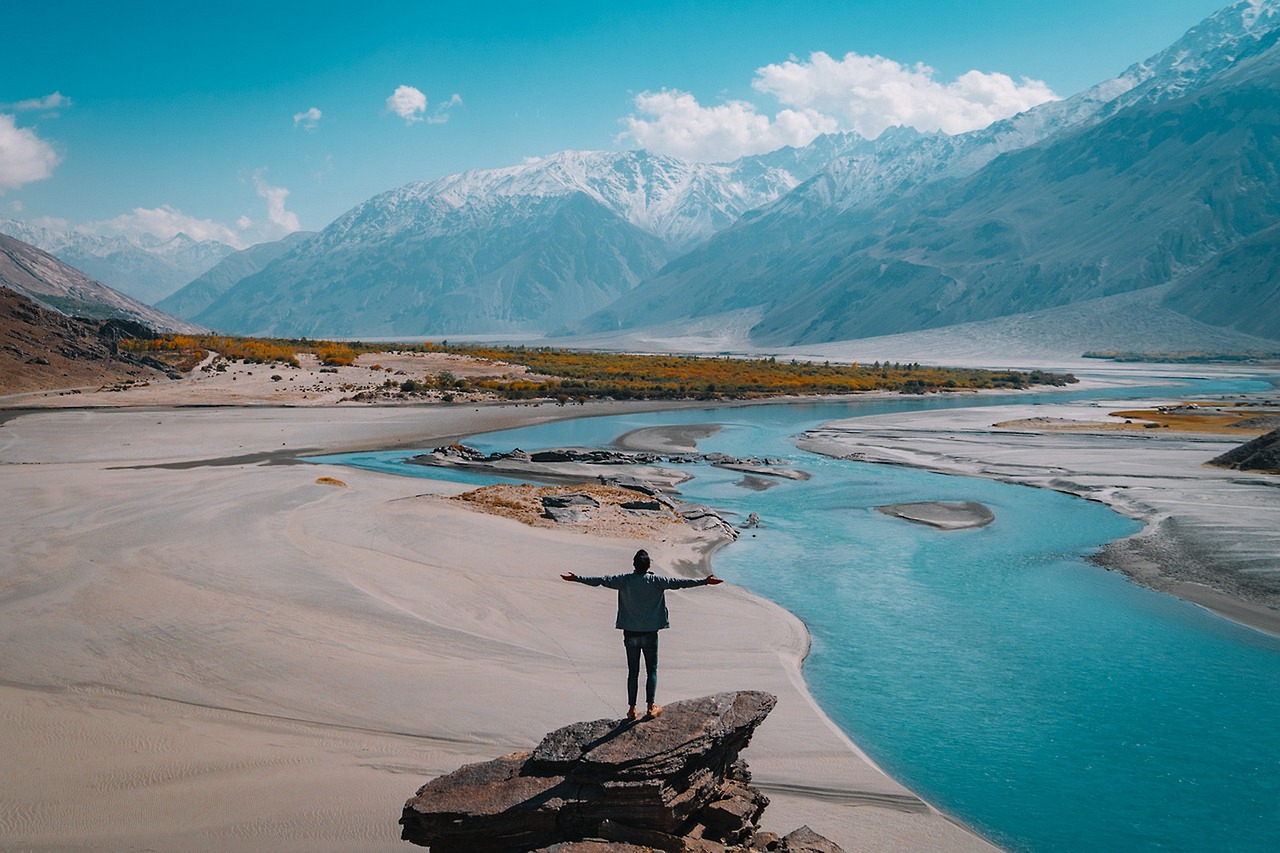 A person standing on a rock overlooking a vast mountain landscape and river, symbolizing the energy flow of the Extraordinary Meridians in Shiatsu.
